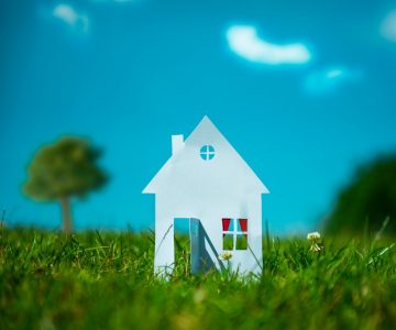 Neubauten: Haus aus Papier auf grüner Wiese