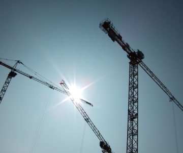 Baukräne vor blauem Himmel mit Sonne
